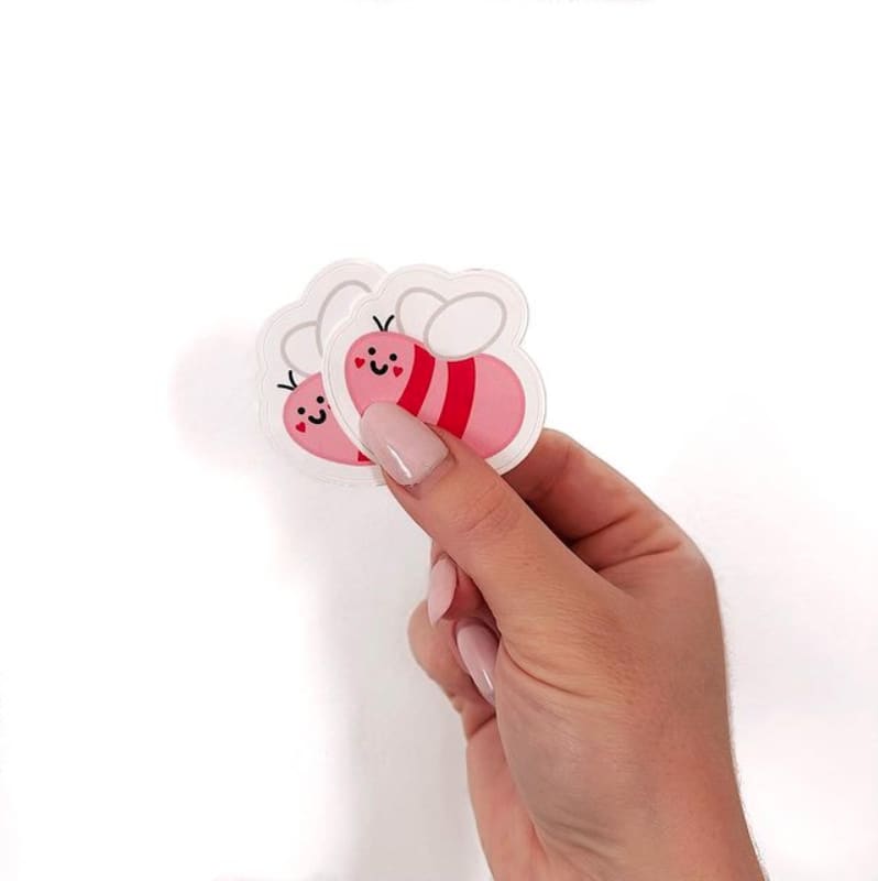 A person holds custom die-cut stickers in the shape of a bee